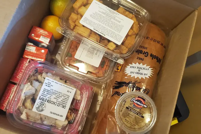 A box containing grilled chicken strips, potatoes, juice boxes, and oranges